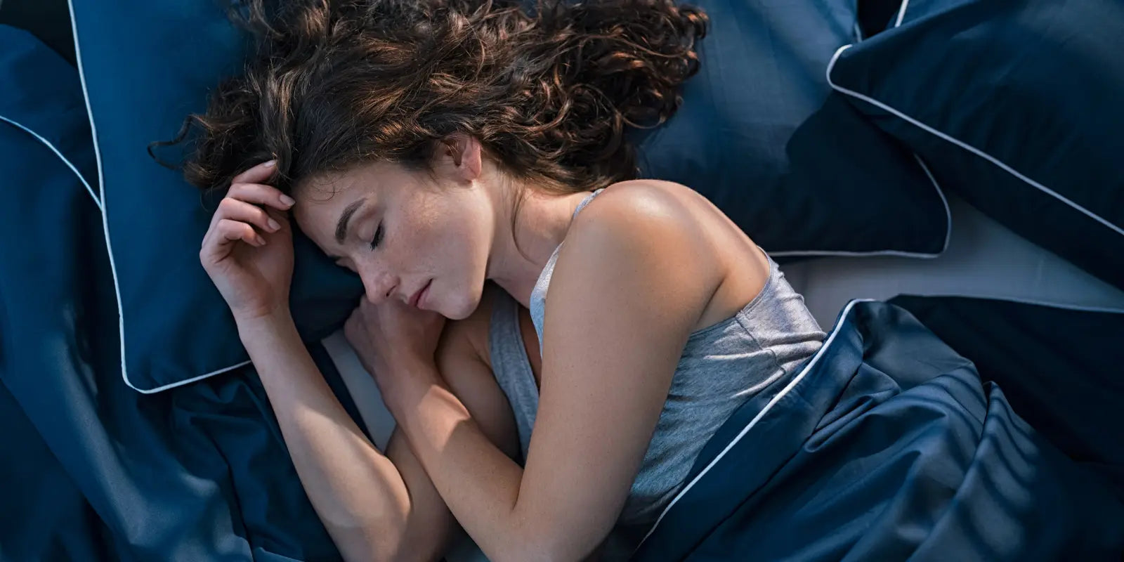 Femme endormie dans un lit avec du linge de lit de couleur bleu marine